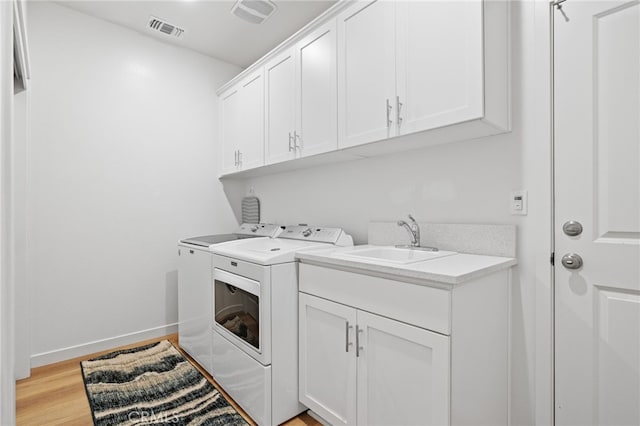 washroom featuring visible vents, light wood finished floors, cabinet space, separate washer and dryer, and a sink