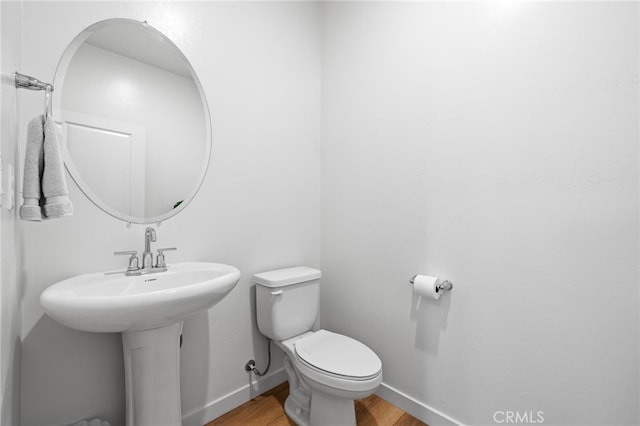 half bath with toilet, baseboards, and wood finished floors