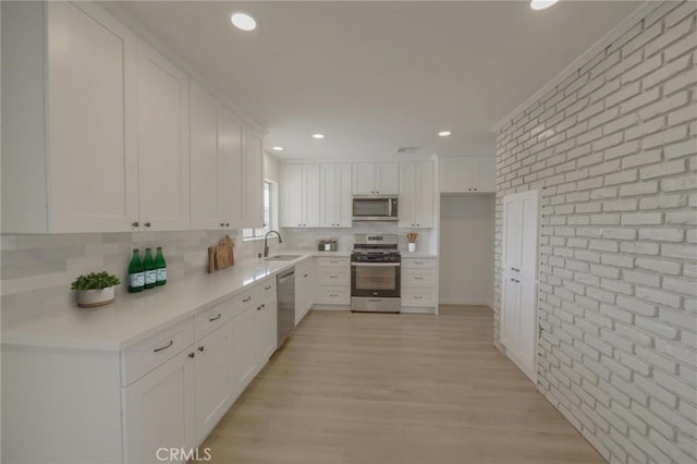 kitchen featuring light wood-type flooring, a sink, white cabinetry, stainless steel appliances, and brick wall