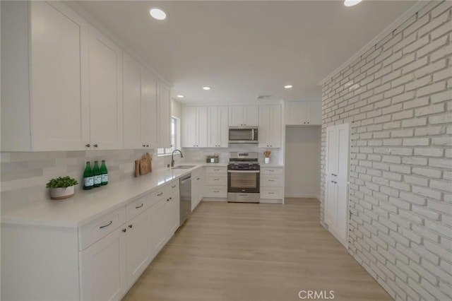 kitchen featuring white cabinets, brick wall, a sink, light countertops, and appliances with stainless steel finishes