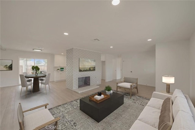 living room featuring a brick fireplace, recessed lighting, and light wood finished floors