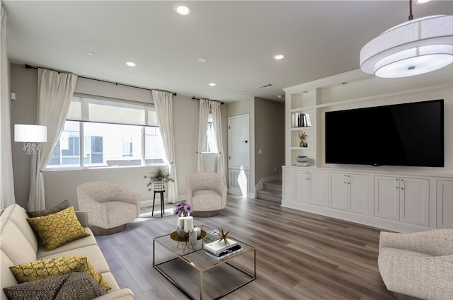 living room featuring built in features, wood finished floors, visible vents, baseboards, and recessed lighting