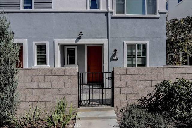 entrance to property with a gate, stucco siding, a balcony, and fence