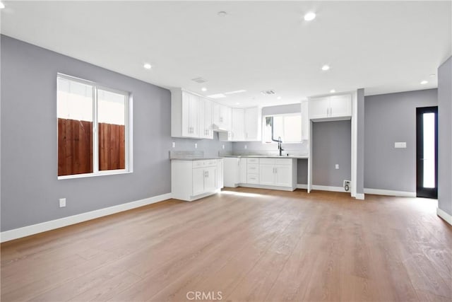 unfurnished living room with a sink, light wood-type flooring, baseboards, and recessed lighting