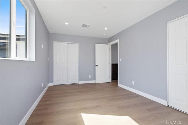 unfurnished bedroom featuring visible vents, baseboards, recessed lighting, wood finished floors, and a closet