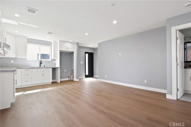 kitchen with light wood finished floors, visible vents, baseboards, under cabinet range hood, and white cabinets