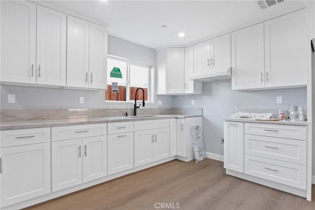 kitchen with visible vents, a sink, light stone counters, white cabinets, and light wood finished floors