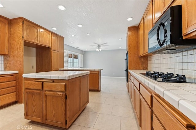 kitchen with ceiling fan, backsplash, black appliances, and tile counters