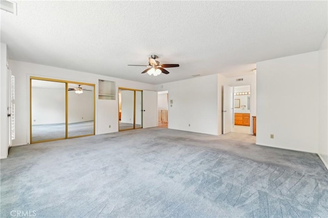 unfurnished bedroom with visible vents, multiple closets, a textured ceiling, and carpet floors