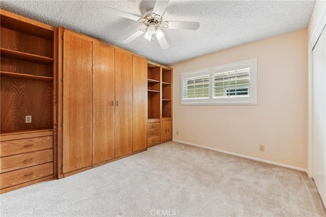 unfurnished bedroom featuring light colored carpet, a textured ceiling, baseboards, and a ceiling fan