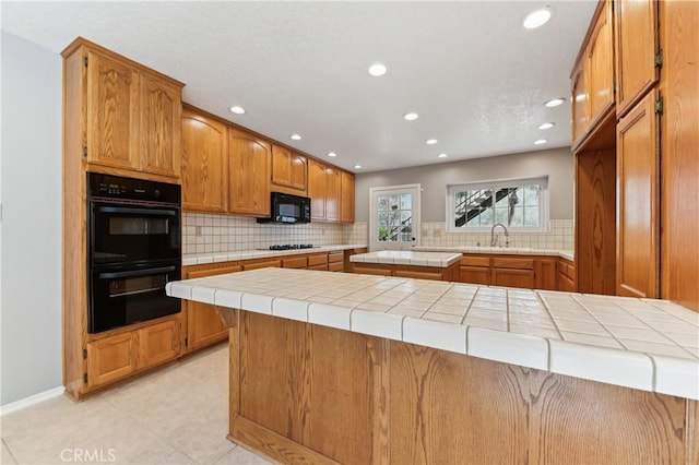 kitchen featuring brown cabinetry, tile countertops, black appliances, and tasteful backsplash