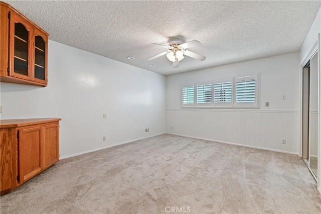 interior space with a textured ceiling, light carpet, a wainscoted wall, and ceiling fan