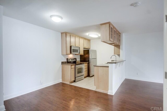 kitchen with glass insert cabinets, light brown cabinetry, light wood-style flooring, a peninsula, and stainless steel appliances