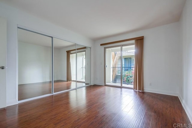 unfurnished bedroom with a closet, wood finished floors, baseboards, and access to exterior