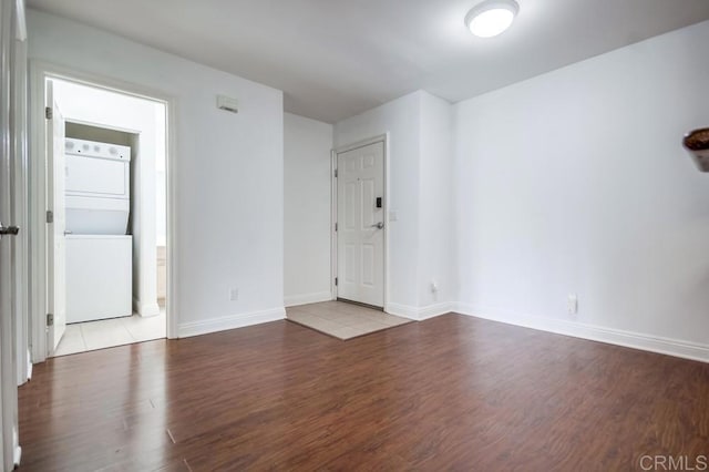 spare room featuring stacked washing maching and dryer, baseboards, and wood finished floors