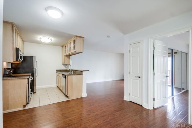 kitchen featuring light wood-type flooring, a sink, dark countertops, stainless steel dishwasher, and range