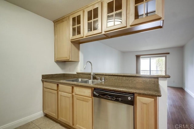 kitchen with light brown cabinetry, a sink, glass insert cabinets, and stainless steel dishwasher