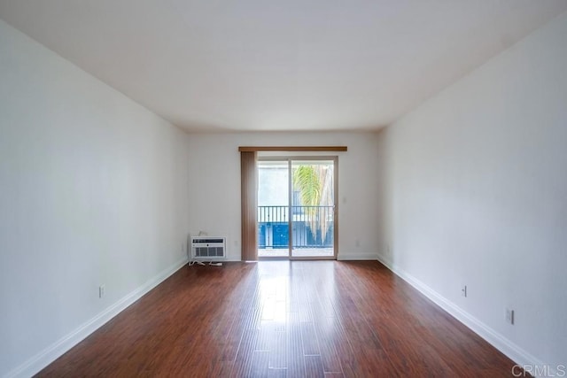 spare room featuring baseboards, an AC wall unit, and dark wood-style floors