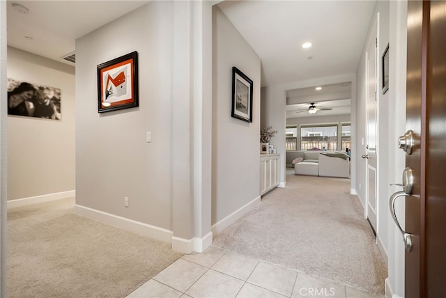 corridor with light tile patterned floors, visible vents, baseboards, and light colored carpet