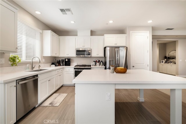 kitchen with visible vents, a kitchen island, a sink, stainless steel appliances, and a kitchen bar