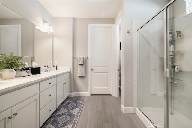 full bath featuring a sink, wood finished floors, a shower stall, double vanity, and baseboards