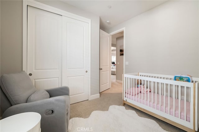 bedroom with a nursery area, light colored carpet, a closet, and baseboards