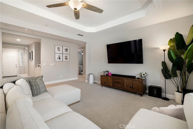 living area featuring visible vents, baseboards, a tray ceiling, light carpet, and a ceiling fan