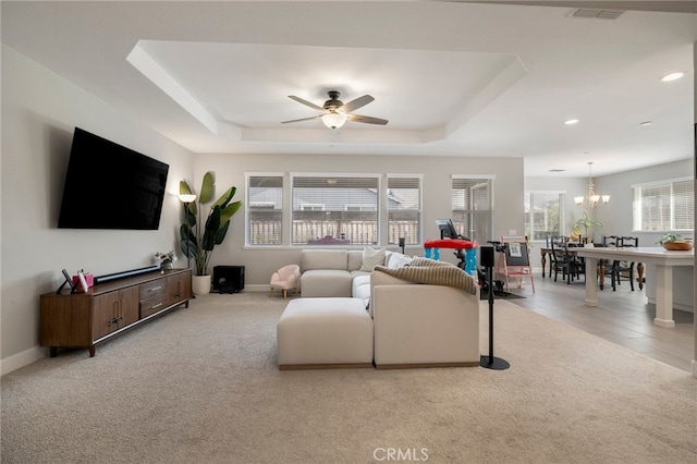 carpeted living room featuring a raised ceiling, ceiling fan with notable chandelier, visible vents, and a healthy amount of sunlight