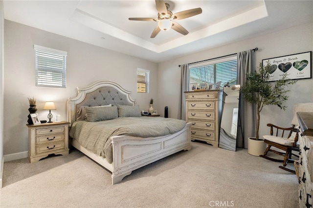 bedroom featuring a ceiling fan, a tray ceiling, and light colored carpet