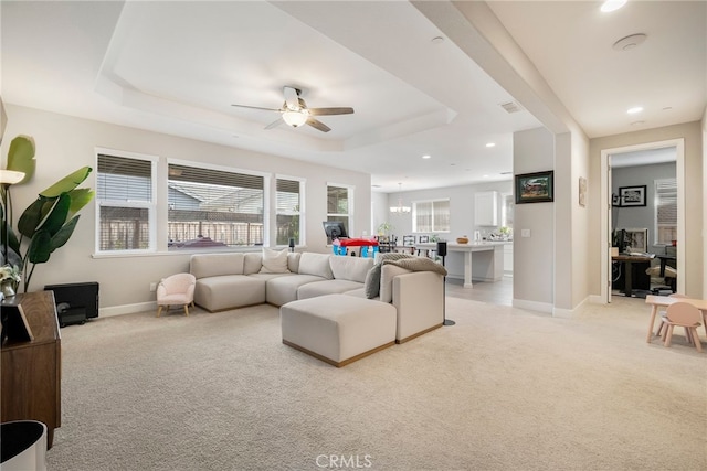 living room with a raised ceiling, plenty of natural light, light carpet, and ceiling fan