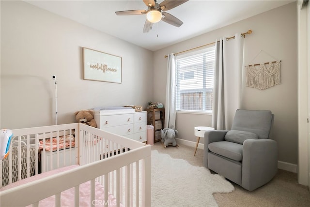 carpeted bedroom featuring baseboards, a nursery area, and ceiling fan