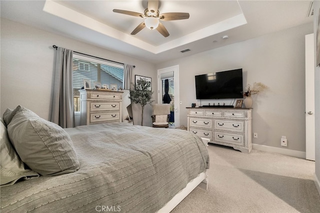 bedroom with light carpet, a ceiling fan, a tray ceiling, baseboards, and a spacious closet