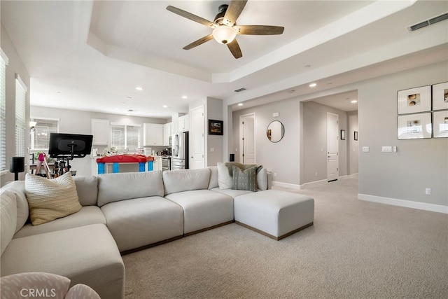 living area with a ceiling fan, a raised ceiling, baseboards, and visible vents