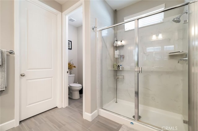 bathroom with a marble finish shower, visible vents, and toilet