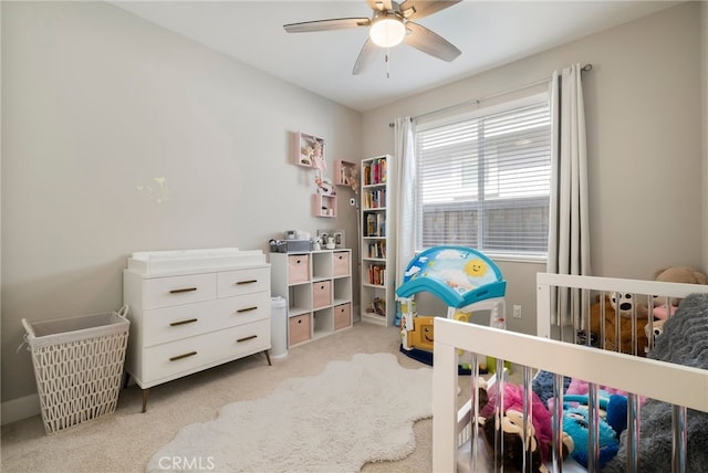 bedroom with ceiling fan, a nursery area, and light carpet