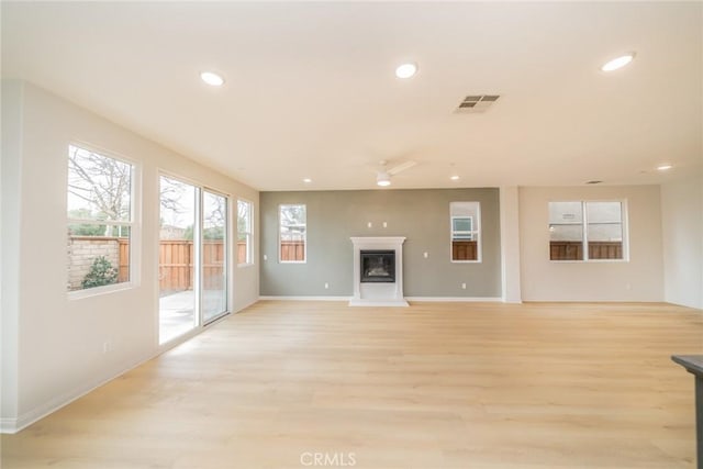 unfurnished living room featuring light wood finished floors, visible vents, recessed lighting, and a glass covered fireplace