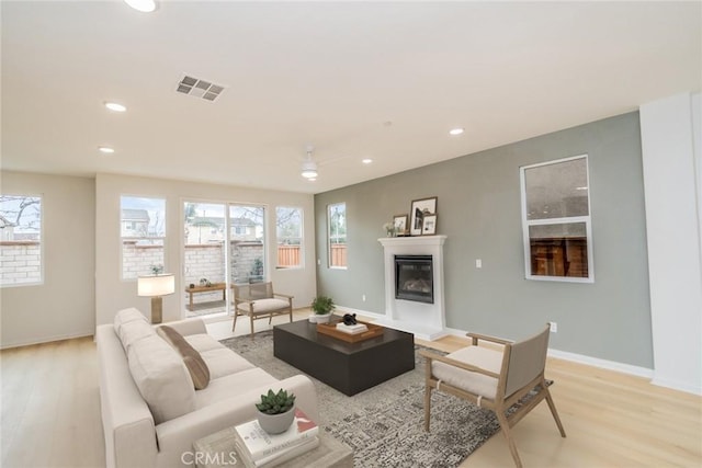 living room with visible vents, recessed lighting, light wood-type flooring, and a glass covered fireplace