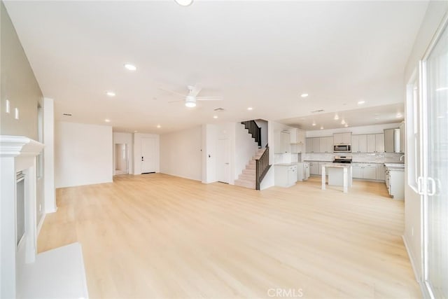 unfurnished living room featuring recessed lighting, stairway, ceiling fan, and light wood finished floors