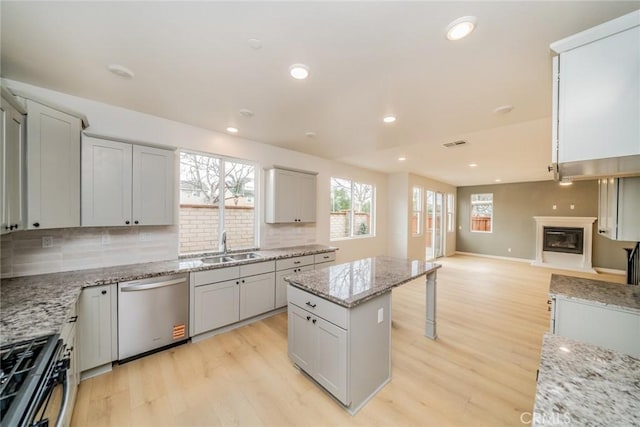 kitchen with a sink, gas stove, light wood-style floors, and stainless steel dishwasher