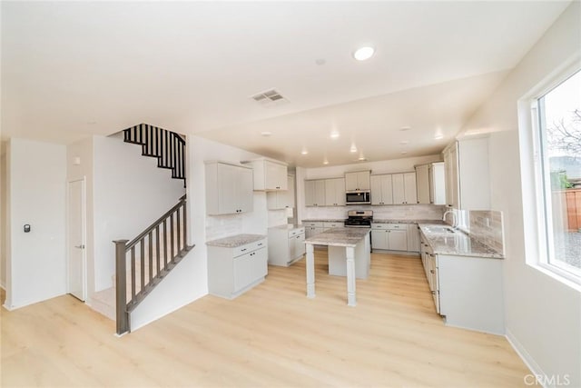 kitchen with light stone countertops, visible vents, a sink, stainless steel appliances, and light wood-style floors