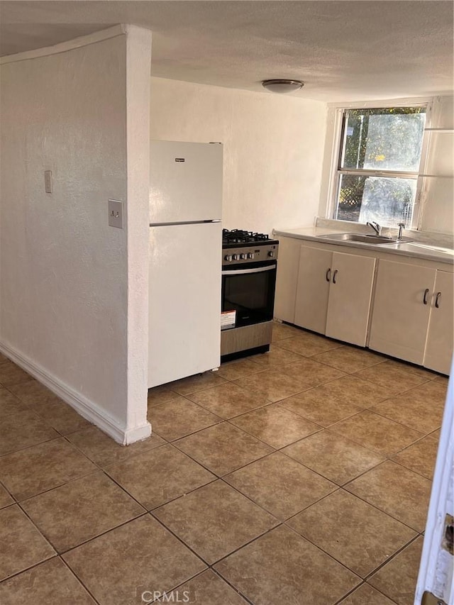 kitchen with stainless steel range with gas cooktop, freestanding refrigerator, a sink, tile patterned flooring, and white cabinets