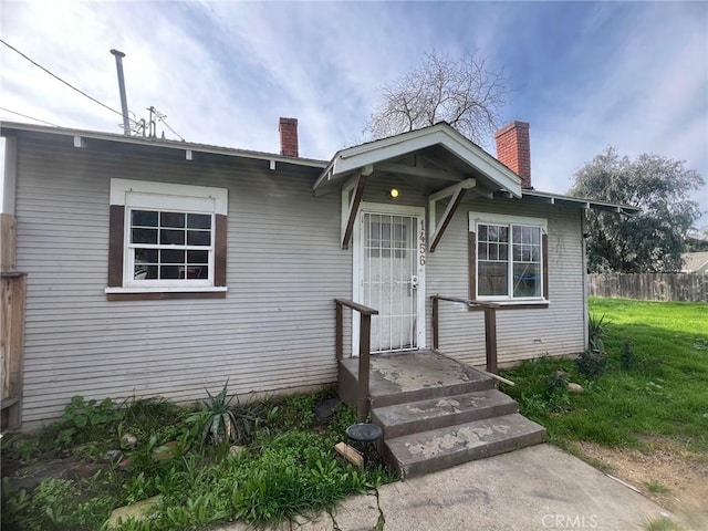 bungalow with a chimney, a front lawn, and fence