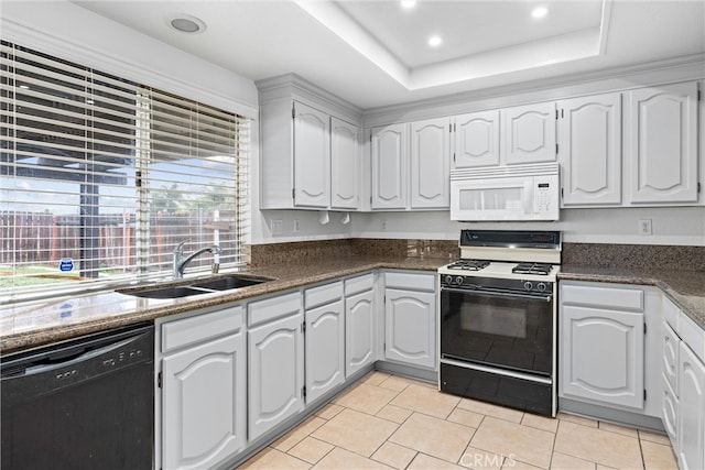 kitchen featuring gas stove, white microwave, a tray ceiling, a sink, and black dishwasher