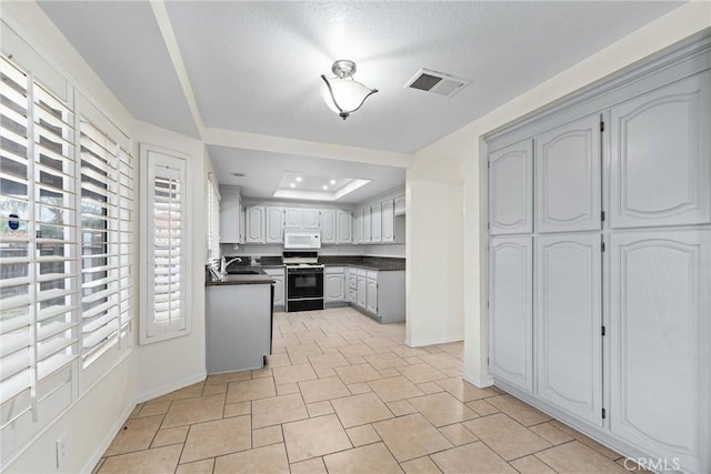 kitchen with white microwave, visible vents, a sink, gas range oven, and dark countertops