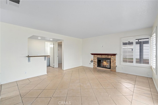 unfurnished living room featuring light tile patterned floors, visible vents, baseboards, and a glass covered fireplace