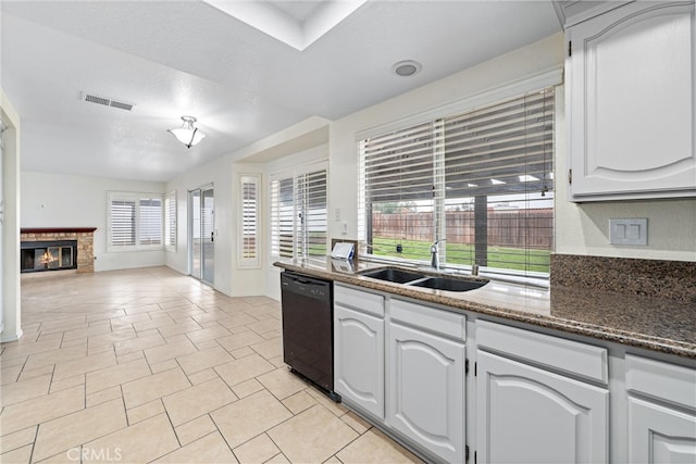 kitchen with visible vents, open floor plan, black dishwasher, a glass covered fireplace, and a sink