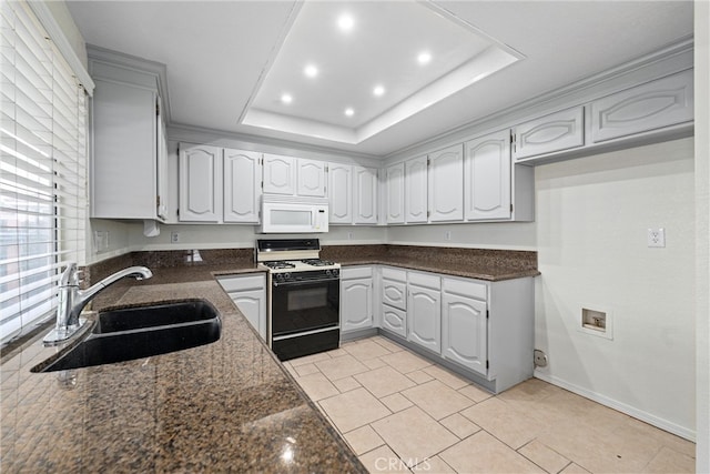 kitchen featuring white microwave, dark stone counters, gas stove, a raised ceiling, and a sink