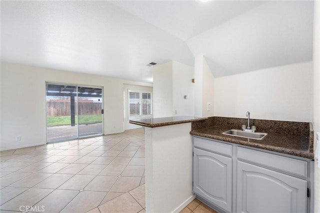 kitchen with a sink, dark stone countertops, a peninsula, light tile patterned floors, and vaulted ceiling