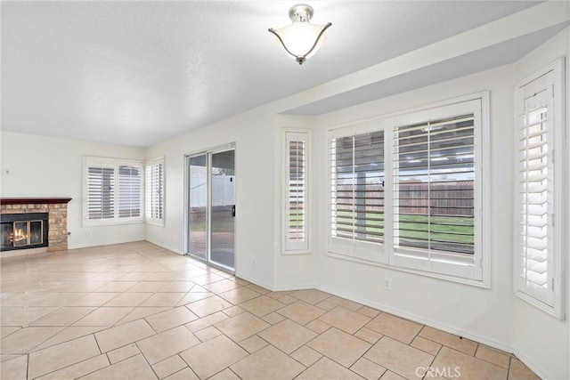 unfurnished living room featuring a glass covered fireplace, light tile patterned floors, baseboards, and a textured ceiling