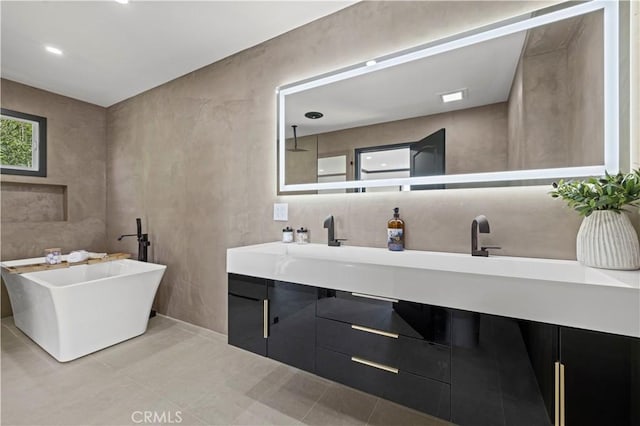 full bathroom with double vanity, a freestanding bath, tile walls, and a sink